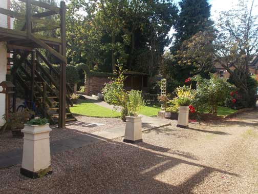 side walk gravel drive lined with ornamental pillars with flower bed tops, with path into gardens